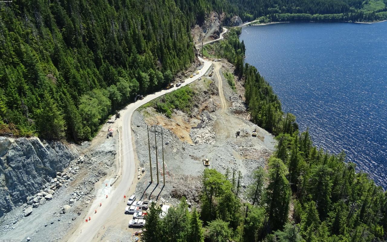 Aerial view of a road winding through forest beside a lake